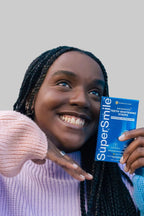 Smiling woman holding SuperSmile Advanced Teeth Whitening Strips